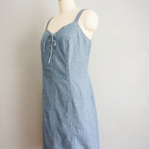 May include: A light blue denim dress with a lace-up detail at the bodice. The dress has a fitted silhouette and a straight hemline.