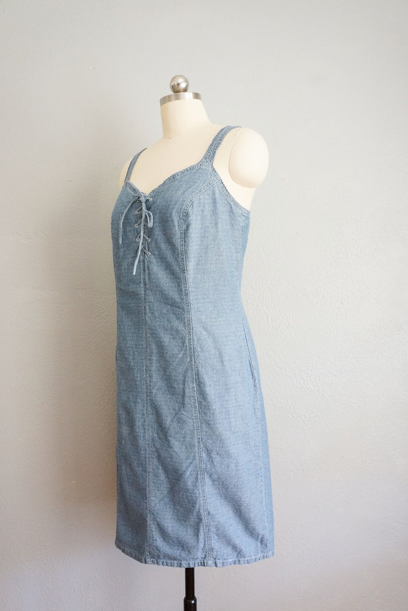 May include: A light blue denim dress with a lace-up detail at the bodice. The dress has a fitted silhouette and a straight hemline.