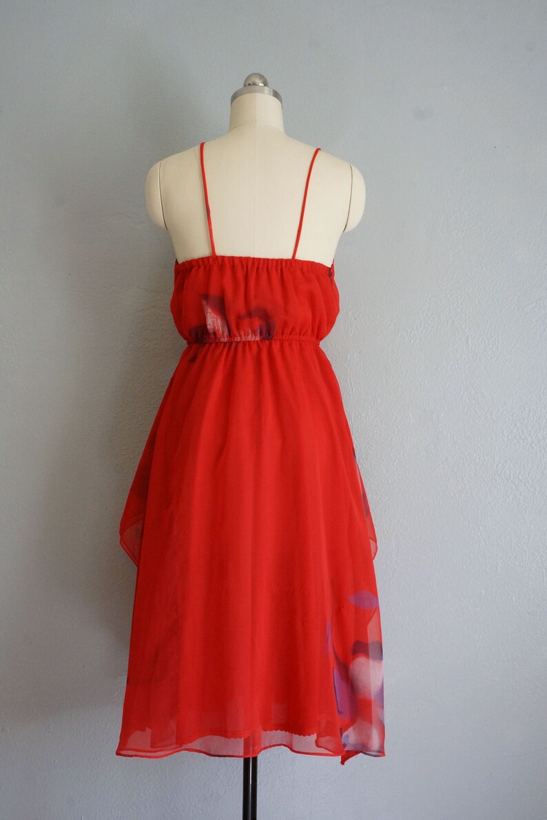 May include: A red sleeveless dress with a floral print. The dress has a gathered waist and a tiered skirt.