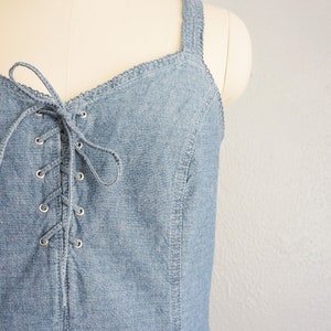May include: A light blue denim dress with a lace-up front and a sweetheart neckline. The dress has thin straps and a fitted bodice.