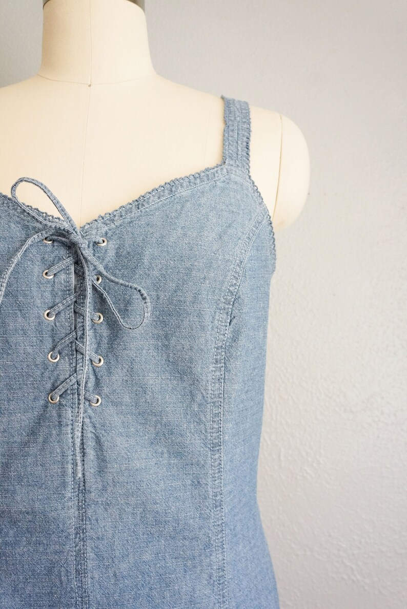 May include: A light blue denim dress with a lace-up front and a sweetheart neckline. The dress has thin straps and a fitted bodice.