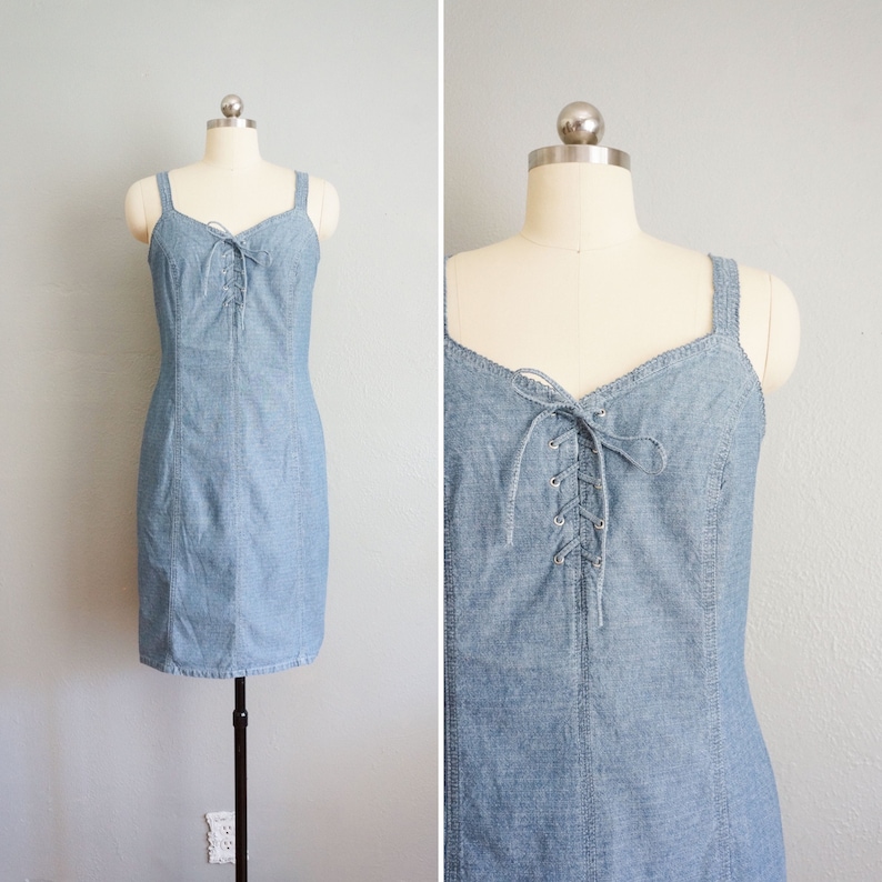 May include: A light blue denim dress with a lace-up detail in the front. The dress has thin straps and a fitted silhouette.