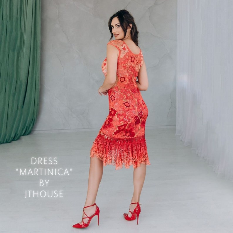 May include: A woman wearing a red and orange crochet dress with a scalloped hem. The dress is called "Martinica" by Jthouse.