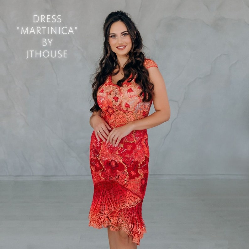 May include: A woman wearing a red and orange crochet dress with a floral pattern. The dress has a fitted bodice and a flowing skirt. The dress is called "Martinique" by Jthouse.