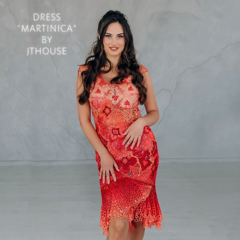 May include: A woman wearing a red and orange crochet dress with a floral pattern. The dress has a fitted bodice and a flowing skirt. The dress is labeled "Dress "Martini&ccedil;a" by JTHouse".