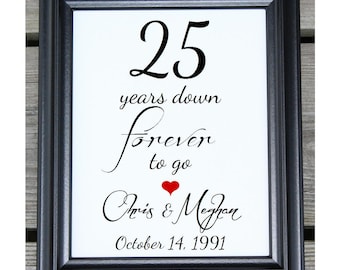 May include: A framed print with black frame and white background. The print says "25 years down forever to go" with a red heart symbol. Below the text is "Chris & Megan" and "October 14, 1991".