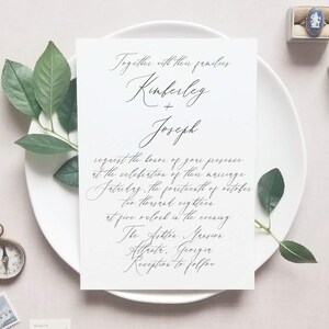 May include: A wedding invitation with a white background and black calligraphy. The invitation reads "Together with their families, Kimberley + Joseph request the honor of your presence at the celebration of their marriage Saturday, the fourteenth of October two thousand eighteen at five o'clock in the evening. The Ashton Mansion Atlanta, Georgia Reception to follow."