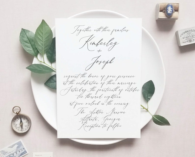 May include: A wedding invitation with a white background and black calligraphy. The invitation reads "Together with their families, Kimberley + Joseph request the honor of your presence at the celebration of their marriage Saturday, the fourteenth of October two thousand eighteen at five o'clock in the evening. The Ashton Mansion Atlanta, Georgia Reception to follow."