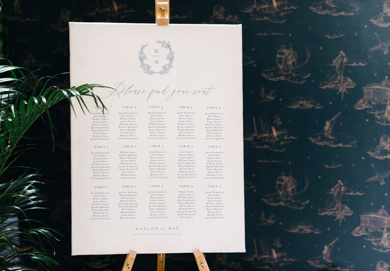 May include: A white seating chart with a blue and white floral wreath with the initials "M & M" at the top. The chart is titled "Please find your seat" and lists names under each table number.