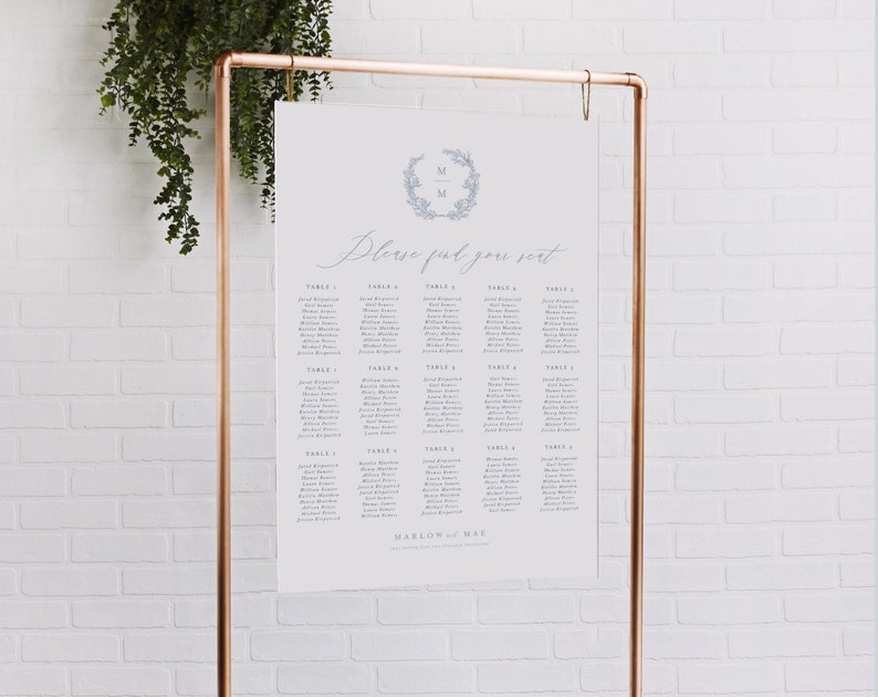 May include: A white wedding seating chart with a blue floral wreath and the initials "M & M" at the top. The chart lists guests' names by table number. The text "Please find your seat" is written in cursive. The chart is displayed on a copper stand.
