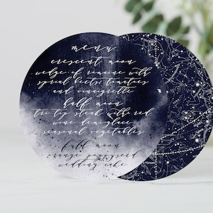 May include: A navy blue and white circular menu card with a watercolor background and a constellation design. The menu features a crescent moon, half moon, and full moon with corresponding food items.
