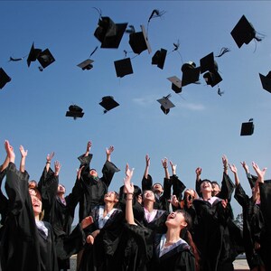 May include: A group of graduates in black caps and gowns throw their caps in the air during a graduation ceremony. The sky is blue and the graduates are smiling and excited.