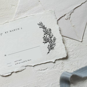 以下が含まれることがあります： 「By March 5」と「can't wait wish we could be there」という黒い文字が書かれた白いRSVPカード。カードには署名用の黒い線と、小さな黒い緑の葉のイラストが描かれている。