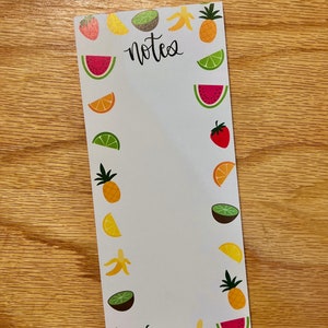 Könnte beinhalten: Ein weißer Notizblock mit einem Rand aus bunten Fruchtillustrationen. Der Notizblock hat das Wort "notes" oben in schwarzer Kursivschrift.