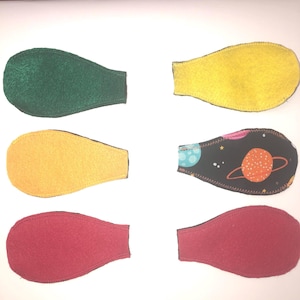 May include: Six eye patches in various colors and patterns. The patches include green, yellow, and red felt, and a black patch with a space-themed design featuring planets and stars. The eye patches are teardrop-shaped.
