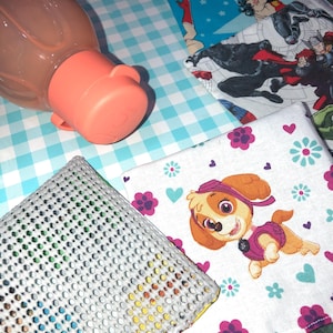 May include: A set of four fabric squares with different designs. The squares are on a blue and white checkered surface. One square features a cartoon dog, another has a superhero theme, and another has a floral pattern. The fourth square is a gray mesh material.