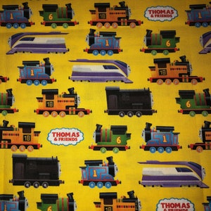 May include: A yellow fabric with a repeating pattern of Thomas the Tank Engine and his friends. The trains are in various colors, including blue, green, red, and yellow. The fabric features the text "Thomas & Friends".