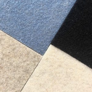 Puede incluir: Primer plano de un dise&ntilde;o geom&eacute;trico compuesto por cuatro cuadrados de fieltro. Los colores son azul claro, negro, blanco roto y un gris-marr&oacute;n claro. El fieltro tiene un aspecto ligeramente texturizado.