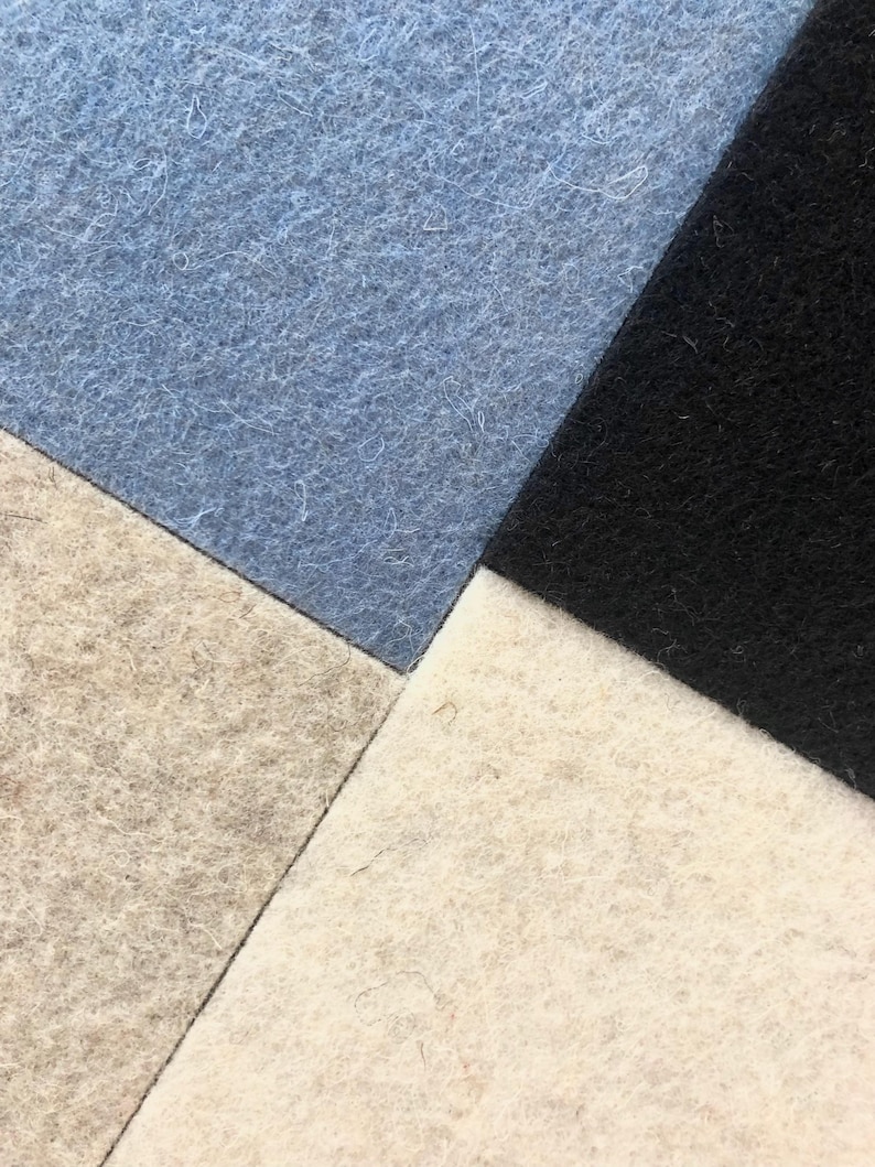Puede incluir: Primer plano de un dise&ntilde;o geom&eacute;trico compuesto por cuatro cuadrados de fieltro. Los colores son azul claro, negro, blanco roto y un gris-marr&oacute;n claro. El fieltro tiene un aspecto ligeramente texturizado.