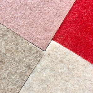 Puede incluir: Primer plano de cuatro cuadrados de tela de fieltro en una disposici&oacute;n geom&eacute;trica. Los colores incluyen rosa claro, rojo, beige y blanco roto. El fieltro tiene un aspecto texturizado y fibroso, con fibras visibles que crean un aspecto suave y t&aacute;ctil. Los cuadrados se encuentran en un punto central.