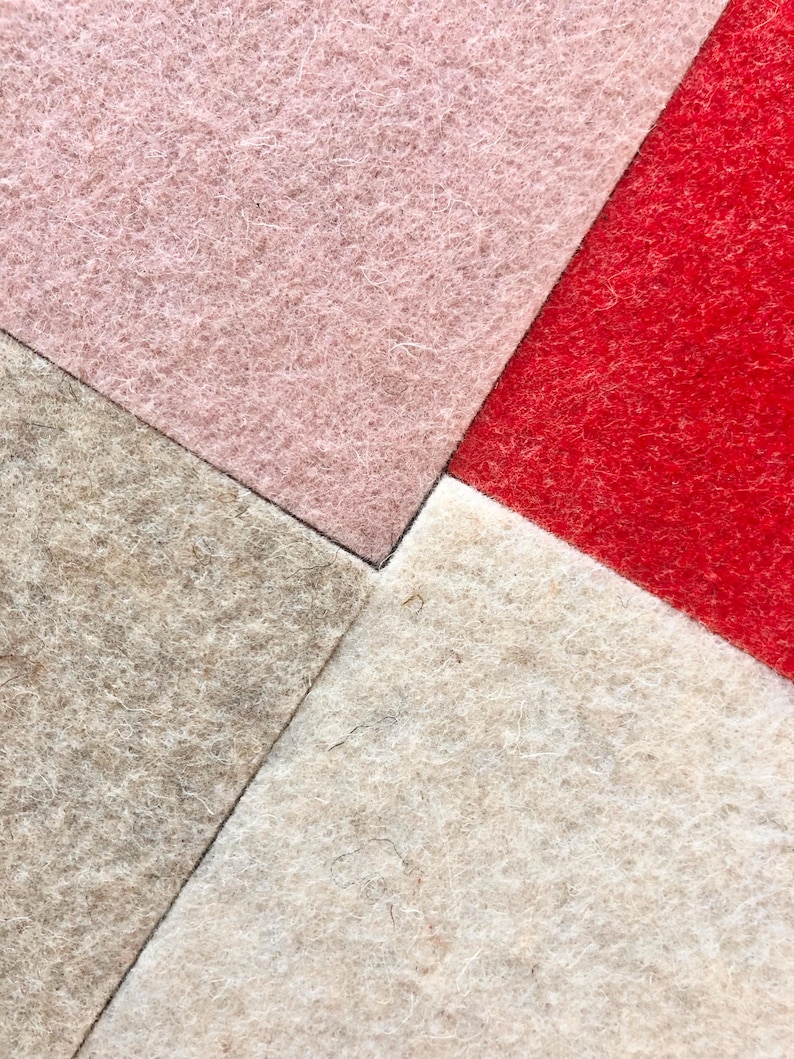 Puede incluir: Primer plano de cuatro cuadrados de tela de fieltro en una disposici&oacute;n geom&eacute;trica. Los colores incluyen rosa claro, rojo, beige y blanco roto. El fieltro tiene un aspecto texturizado y fibroso, con fibras visibles que crean un aspecto suave y t&aacute;ctil. Los cuadrados se encuentran en un punto central.