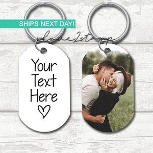 May include: Two silver keychains with a white oval tag. One tag has the text "Your Text Here" with a heart symbol. The other tag has a photo of a couple embracing.