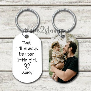 May include: A set of two silver keychains. One keychain has a white oval tag with the text "Dad, I'll always be your little girl. ♡ Daisy". The other keychain has a white oval tag with a photo of a father and daughter.