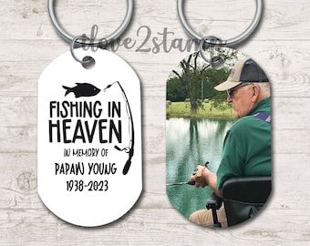 May include: A white oval keychain with a black fishing rod and fish design. The text reads "Fishing in Heaven" in memory of "Papaw Young" 1938-2023. The other side of the keychain features a color photo of a man fishing.