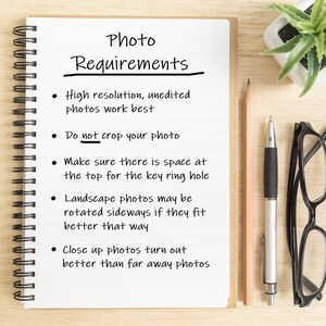 May include: A white notebook with a black spiral binding and lined pages. The notebook has handwritten instructions for taking photos, including "Photo Requirements", "High resolution, unedited photos work best", "Do not crop your photo", "Make sure there is space at the top for the key ring hole", "Landscape photos may be rotated sideways if they fit better that way", and "Close up photos turn out better than far away photos".