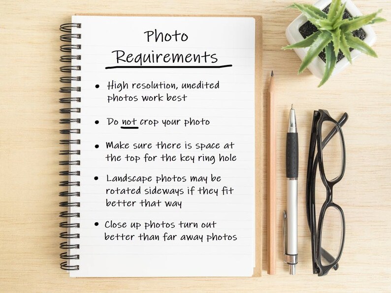 May include: A white notebook with a black spiral binding and lined pages. The notebook has handwritten instructions for taking photos, including "Photo Requirements", "High resolution, unedited photos work best", "Do not crop your photo", "Make sure there is space at the top for the key ring hole", "Landscape photos may be rotated sideways if they fit better that way", and "Close up photos turn out better than far away photos".