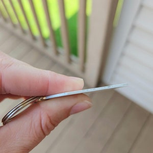 以下が含まれることがあります： 丸いタグが付いた銀色の金属製のキーホルダー。タグは空白で、表面が滑らかです。