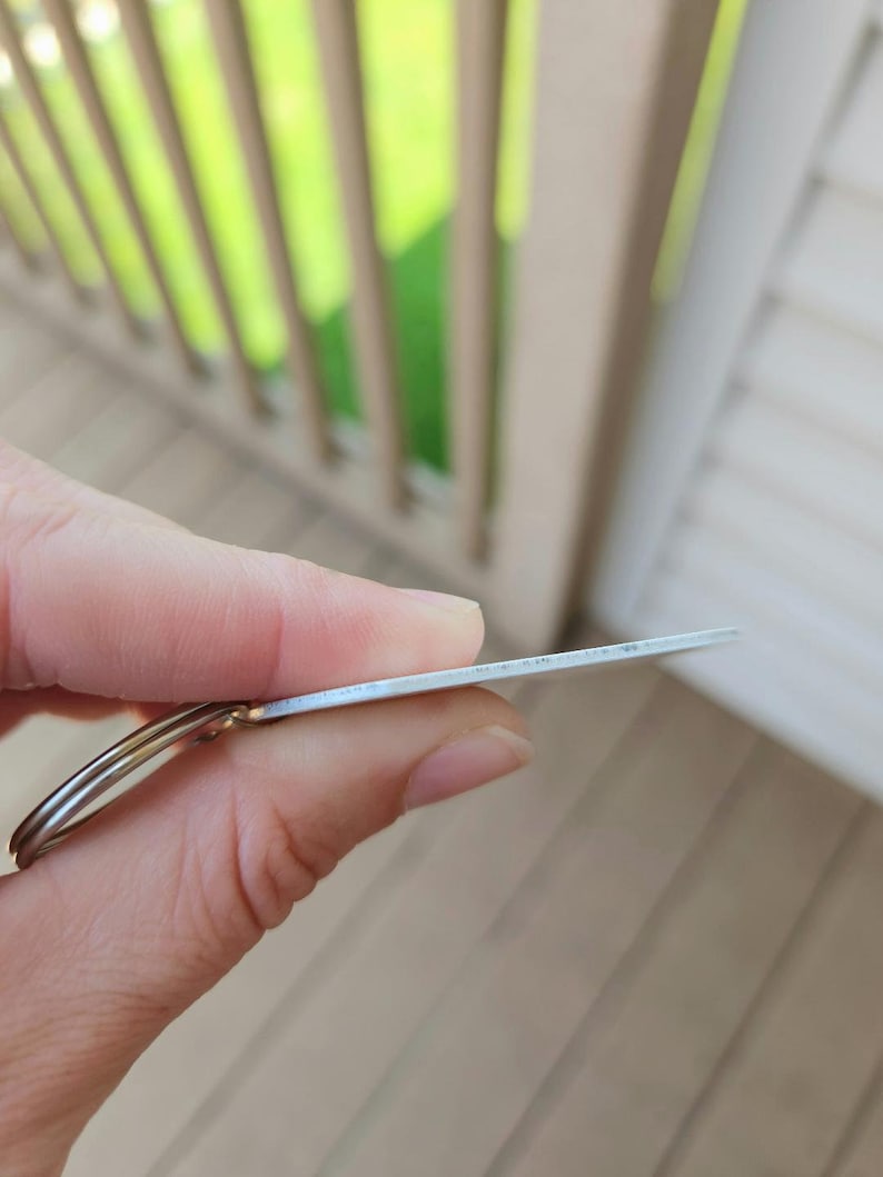 以下が含まれることがあります： 丸いタグが付いた銀色の金属製のキーホルダー。タグは空白で、表面が滑らかです。