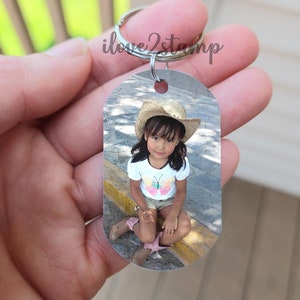 Peut inclure: Un porte-cl&eacute;s argent&eacute; avec une photo d'une jeune fille portant un chapeau de paille et une chemise &agrave; papillon. La photo est sur une &eacute;tiquette rectangulaire.