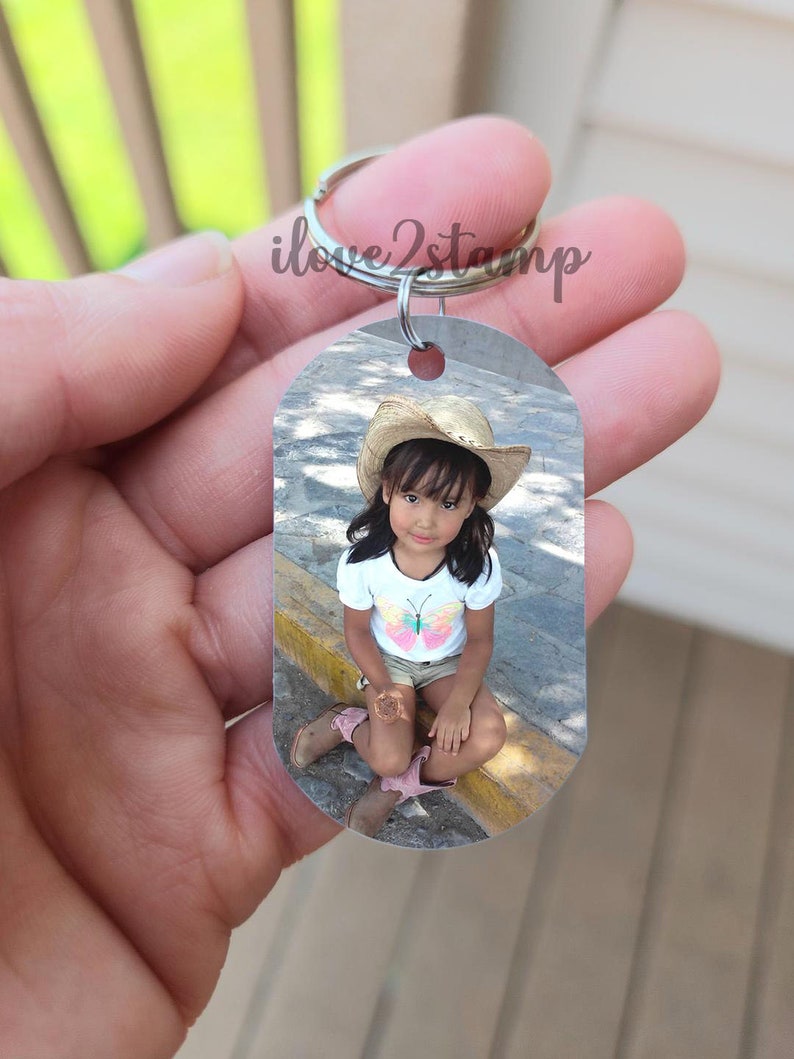 Peut inclure: Un porte-cl&eacute;s argent&eacute; avec une photo d'une jeune fille portant un chapeau de paille et une chemise &agrave; papillon. La photo est sur une &eacute;tiquette rectangulaire.