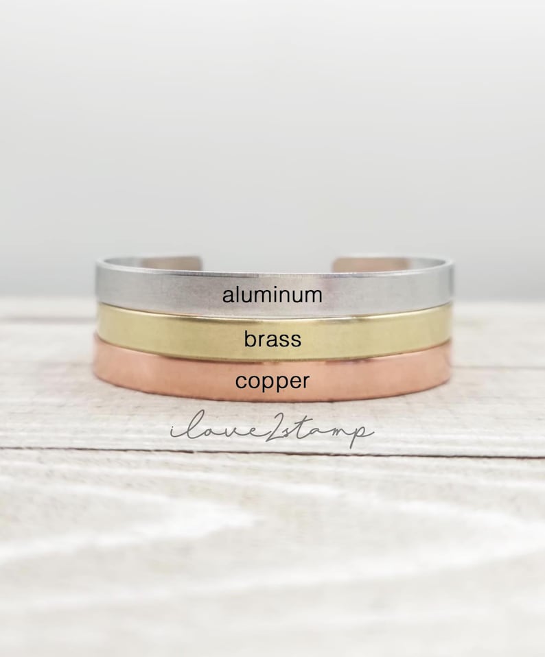 May include: Three stacked bracelets in different metals: aluminum, brass, and copper. The bracelets are all plain and have the words "aluminum", "brass", and "copper" engraved on them.