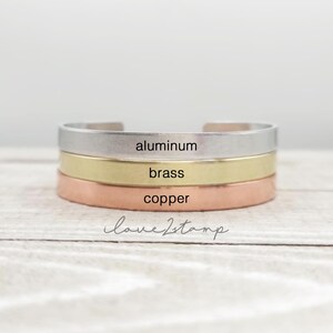 May include: Three stacked bracelets in different metals: aluminum, brass, and copper. The bracelets are all plain and have the words "aluminum", "brass", and "copper" engraved on them.