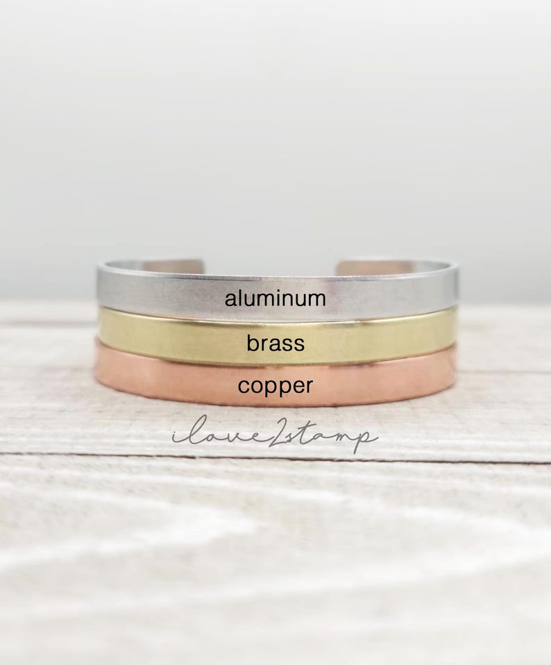 May include: Three stacked bracelets in different metals: aluminum, brass, and copper. The bracelets are all plain and have the words "aluminum", "brass", and "copper" engraved on them.