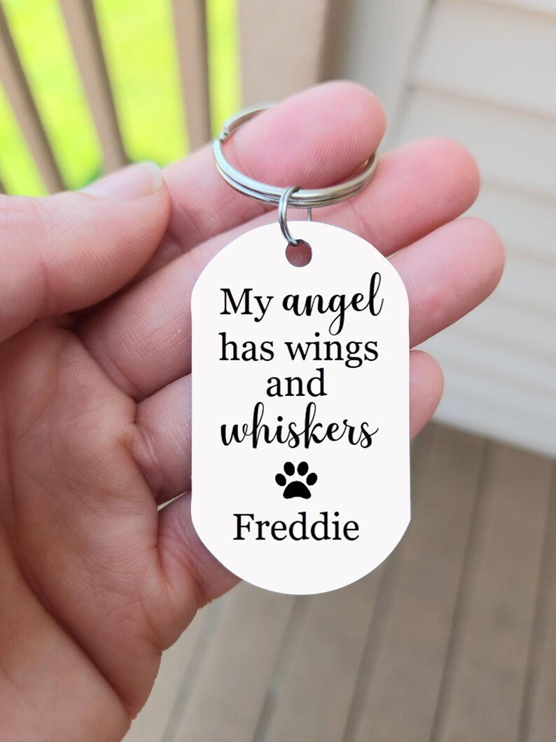 May include: White metal keychain with the text "My angel has wings and whiskers" and a paw print. The name "Freddie" is printed below the paw print.
