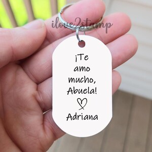 Peut inclure: Porte-cl&eacute;s ovale blanc avec le texte "&iexcl;Te amo mucho, Abuela!" et un symbole de c&oelig;ur. Le nom "Adriana" est &eacute;crit sous le c&oelig;ur.