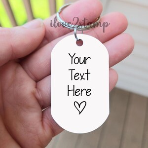 K&ouml;nnte beinhalten: Wei&szlig;er ovaler Schl&uuml;sselanh&auml;nger mit einem silbernen Ring. Der Schl&uuml;sselanh&auml;nger tr&auml;gt den Text "Your Text Here" und ein kleines Herz.