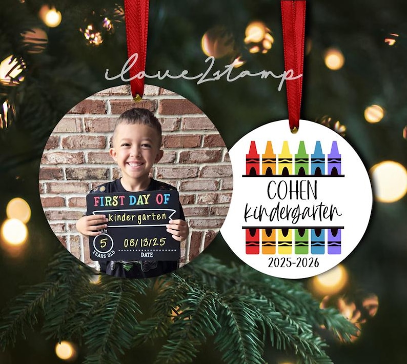 Op de afbeelding: Twee ronde keramische ornamenten met rode linten. E&eacute;n ornament toont een foto van een kind met een schoolbordje met de tekst FIRST DAY OF kindergarten 5 YEARS OLD 08/13/25. De andere toont kleurrijke kleurpotloodafbeeldingen, de naam COHEN, de tekst kindergarten en 2025-2026.
