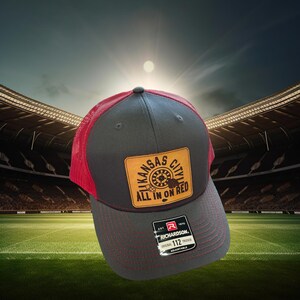 May include: Gray and red trucker hat with a brown leather patch that says "Kansas City All In On Red". The patch has a roulette wheel design. The hat is adjustable and has a Richardson logo.