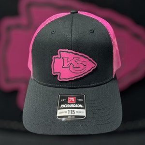 Puede incluir: Gorra de camionero negra y rosa con un logotipo rosa de los Kansas City Chiefs. La gorra tiene una parte trasera de malla y una visera negra. La gorra tiene un logotipo de Richardson y el texto "EST. 1970" y "LOW-PRO 115 TRUCKER" en la parte delantera.