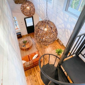 May include: A white cabin interior with a spiral staircase, a brown leather couch, and two large woven pendant lights.