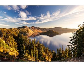 May include: A scenic landscape photograph of a lake surrounded by mountains and evergreen trees under a blue sky with wispy clouds. The water reflects the sky and surrounding landscape, creating a serene and natural scene.