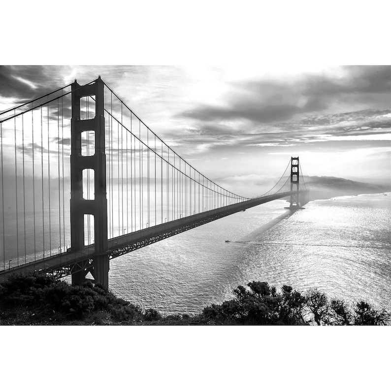 May include: A black and white photograph of the Golden Gate Bridge in San Francisco, California. The bridge is a suspension bridge with two towers and a long span. The bridge is seen from a distance, with the water and fog in the background.