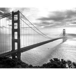 May include: A black and white photograph of the Golden Gate Bridge in San Francisco, California. The bridge is seen from a distance, with the fog rolling in over the water.