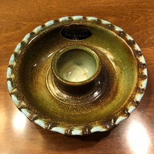 May include: A green and brown ceramic serving dish with a blue rim and a smaller, round bowl in the center. The dish has a scalloped edge and a label that reads "Potters Wheel Original".