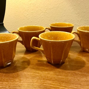 May include: Set of five brown ceramic teacups with a speckled glaze. The cups have a flared shape and a rounded handle.