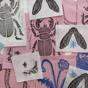 May include: A collection of fabric squares with various black and white linocut prints of insects, plants, and other designs. The prints are on a variety of colored fabrics, including pink, blue, and white.